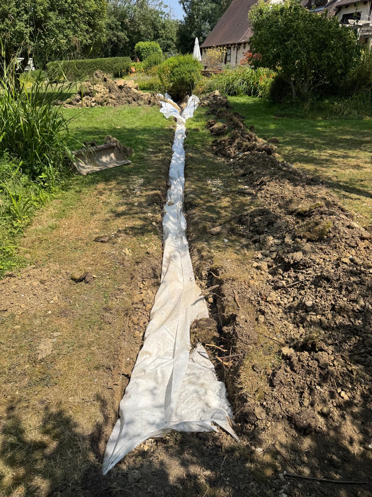 Membrane-lined drainage trench running across a lawn towards the ditch