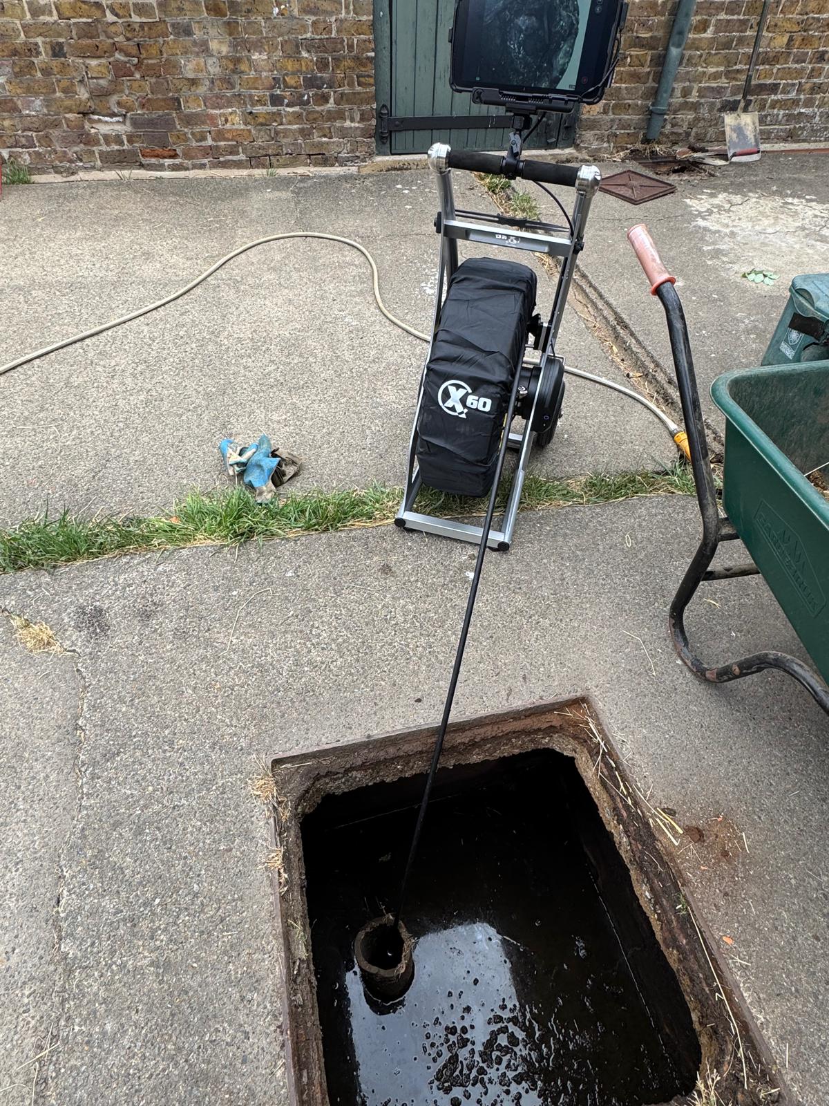CCTV drain camera reel positioned on a concrete yard beside an open inspection chamber, with the camera cable fed down into the chamber