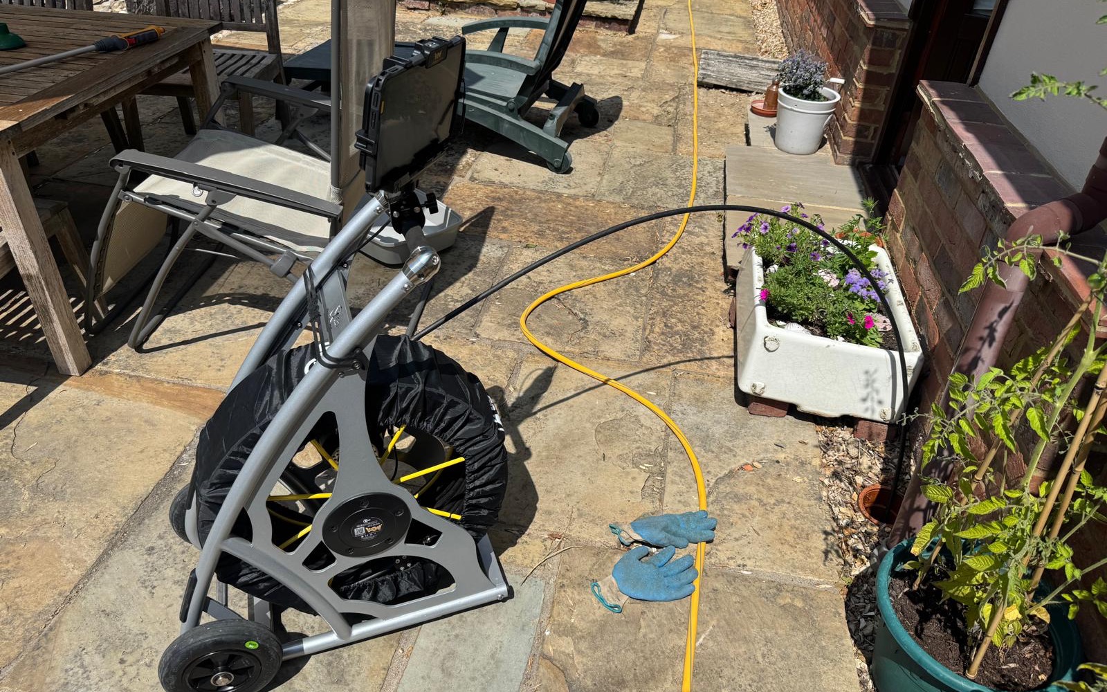 Flowcraft CCTV drain survey reel on a stone patio, with the camera cable running across to a drain beside the house wall