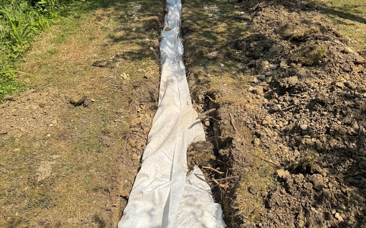 Open drainage trench across a lawn, lined with white filter fabric and not yet backfilled