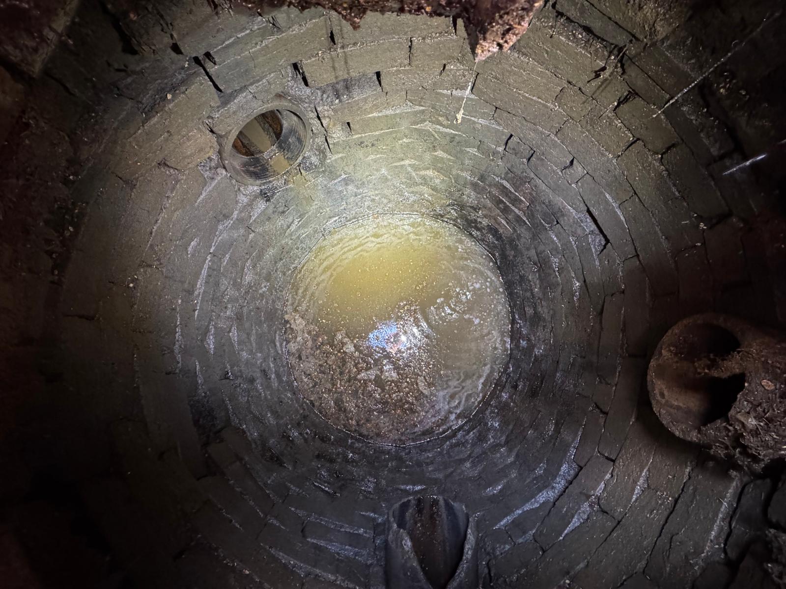 Inside an old round brick wastewater chamber with inlet pipes and solids at the base, seen during a drainage survey