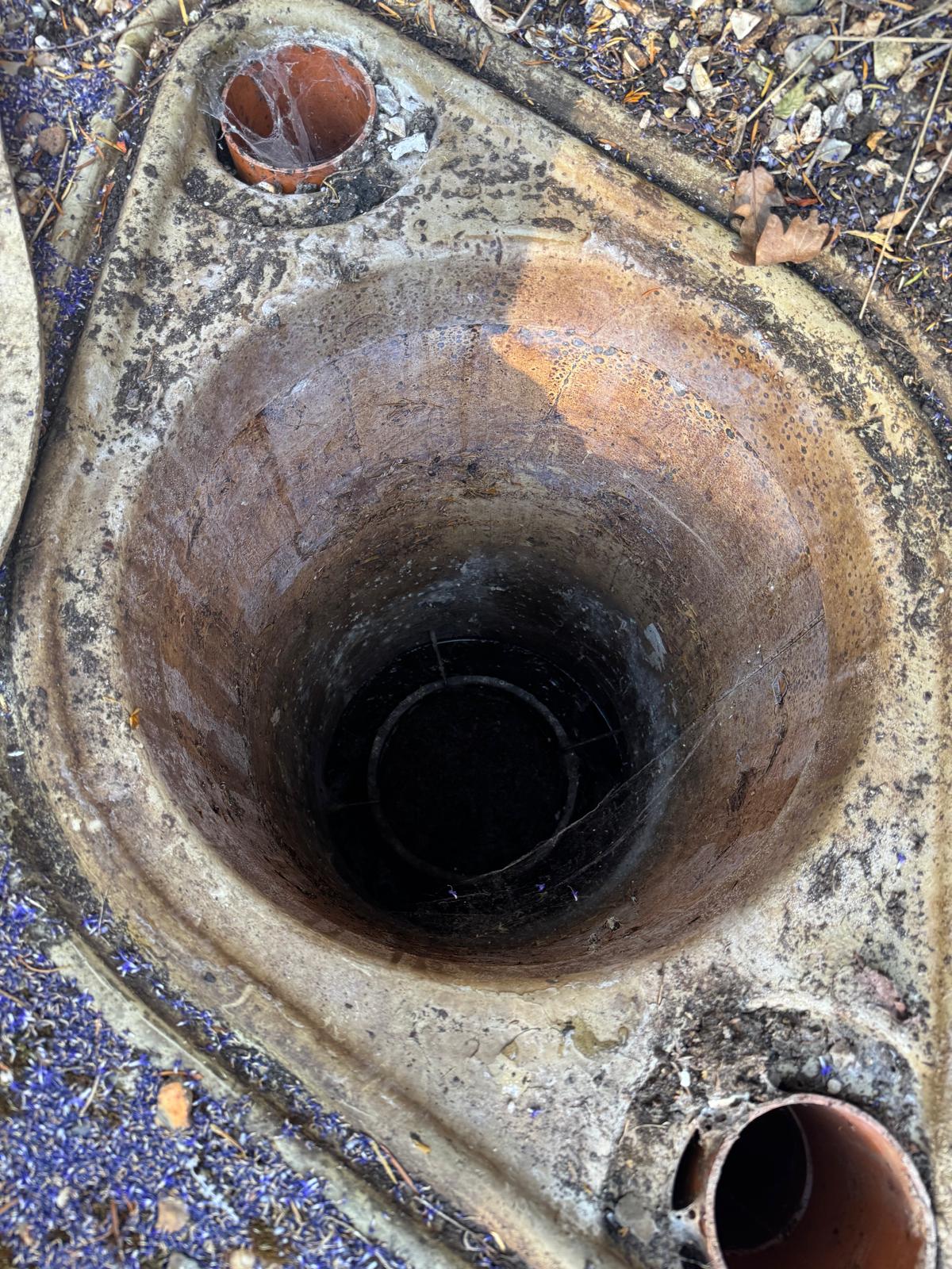 Open neck of a buried plastic wastewater tank with orange pipe connections, inspected during a septic tank survey